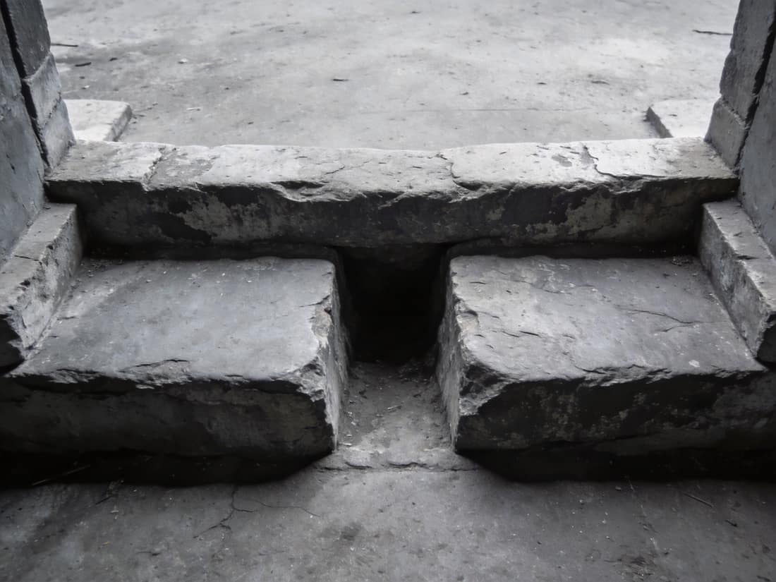A worn stone threshold seen from above, its hollow far deeper on one side than the other