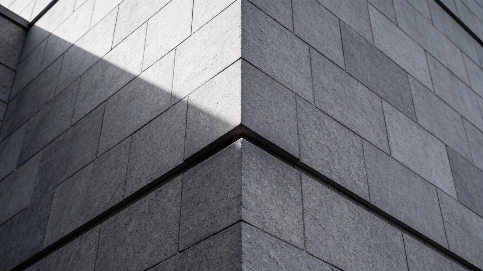 The external corner of a severe ashlar building where two elevations meet on a sharp quoined edge, one face brighter than the other
