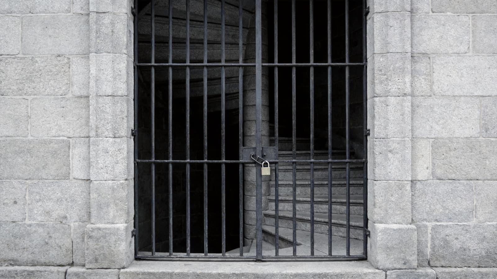 A single heavy panelled door closed at the end of a dim stone corridor, a strip of cold daylight beneath it